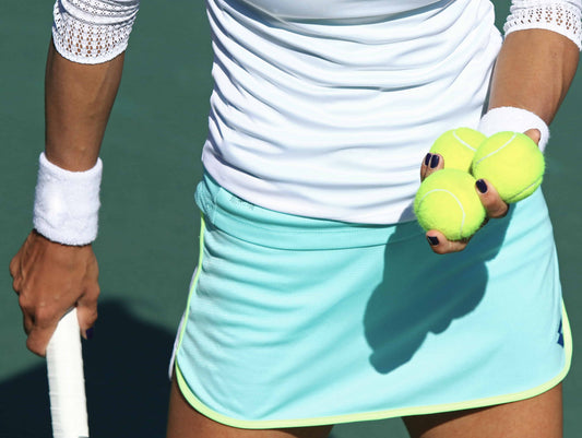 Woman ready to serve with three tennis balls in her hand.