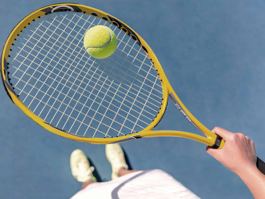 Woman balancing tennis ball on racquet above court